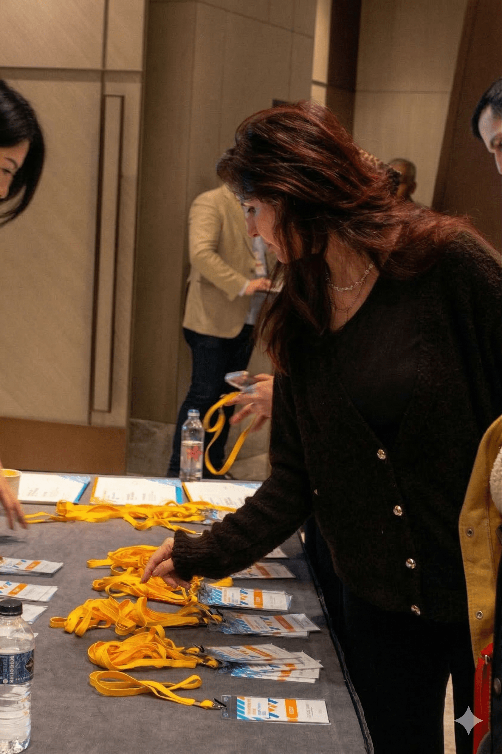Woman with reddish hair picks up yellow lanyards from an event registration table.