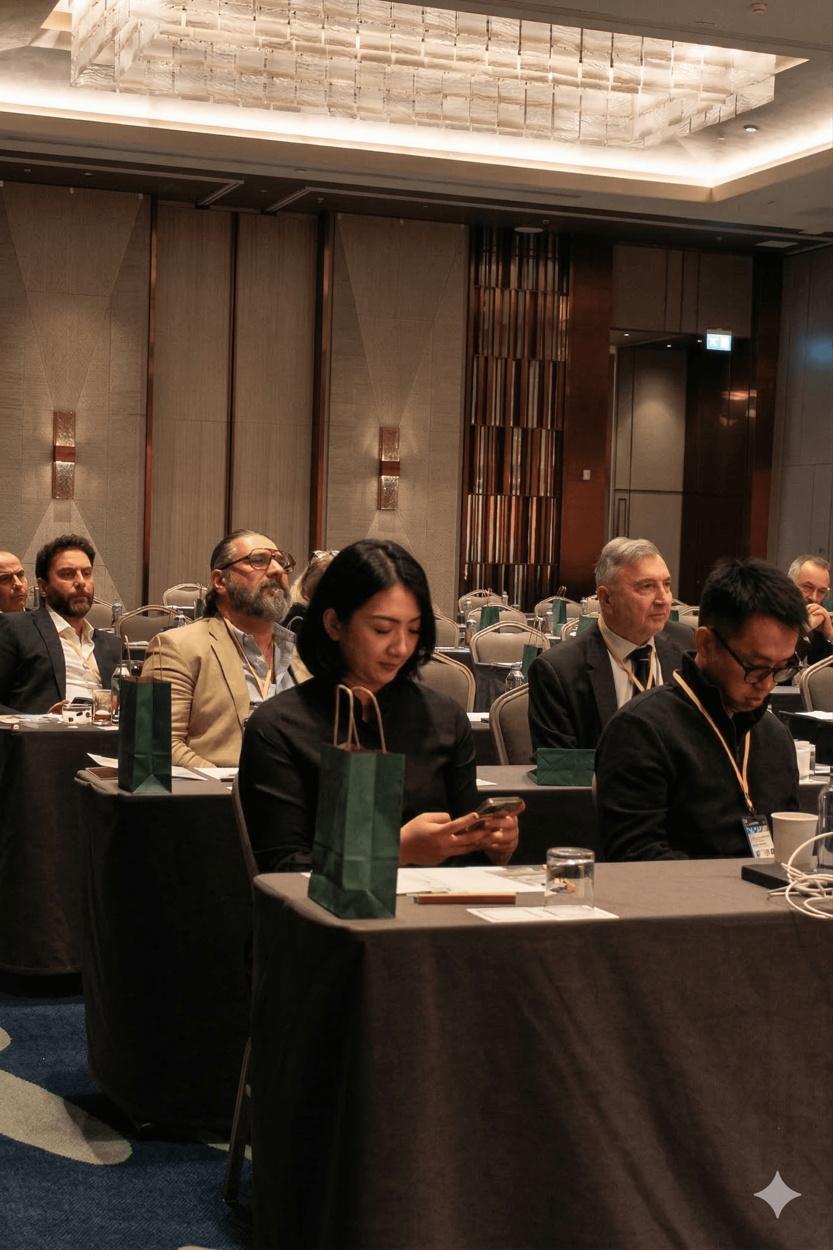Attendees seated at a professional conference, with a woman in the foreground using her phone.